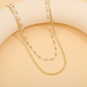 Detail der zwelagigen Gold-Schlangenkette und Perlenkette auf einem minimalistischen Ständer