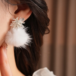 Close-up of snowflake silver earring with white pompom worn by a model in soft light