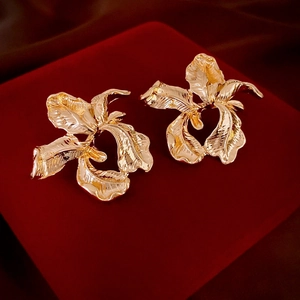 Detailed view of golden flower earrings with petal texture on deep red velvet