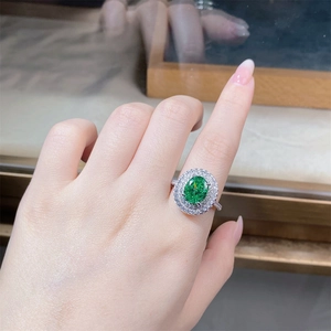 Detailed view of an oval green gemstone ring with a diamond halo on a model hand