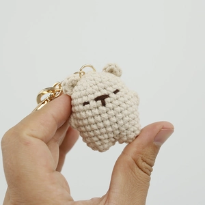 Handmade knitted beige bear keychain with golden metal ring on a white background