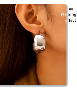 Wearing effect of large polished silver C-shaped chunky hoop earrings on model ear
