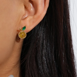 Detailed close-up of a model wearing a small yellow lemon-shaped stud earring with green leaf