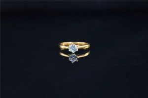 Detail of a six-prong moissanite ring with a gold band reflecting on a black surface