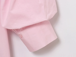 Close-up of light pink cotton shirt cuff featuring a single button and pleated details