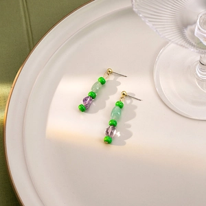 Detailed shot of green and purple beaded earrings with gold tassels on a beige tray