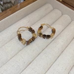 Macro detail of vintage square tiger eye stone charms on golden metal hoop earrings