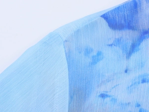 Dettaglio ravvicinato della camicia in chiffon azzurra con stampe e trama del tessuto