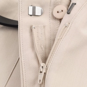 Detailed close-up of high waist closure with zipper, button and metal hook on beige trousers