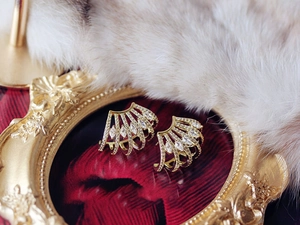 Macro shot of gold-plated fan-shaped earrings with zircon inlay on a white fur background