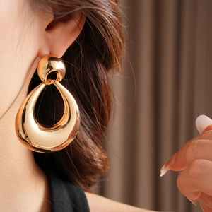 Close-up of model wearing large golden teardrop earrings in a minimalist fashion style