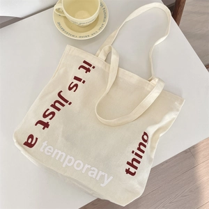 Détail du sac cabas en toile avec texte bordeaux imprimé it is just a temporary thing