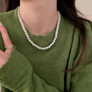 Gros plan d'un collier de perles blanches et bague dorée sur pull en maille verte