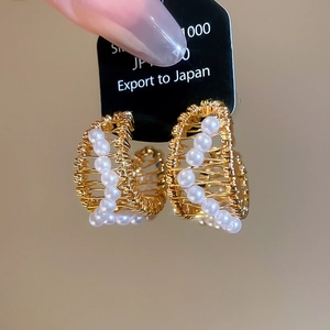 Detail of 18k gold plated C-shape earrings featuring woven pearls and intricate texture