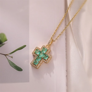Detailed view of a gold cross pendant with emerald green zircons and white crystals