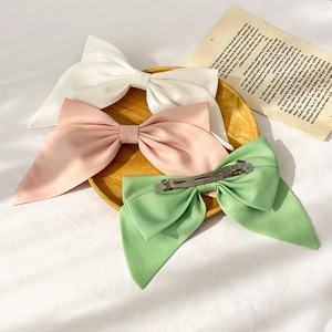 Flat lay of satin bow hair clips in white, pink, and green on a minimalist background