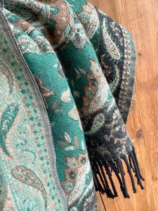 Close-up of green and brown paisley woven shawl with detailed fringe on wood surface