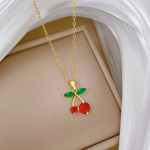 Close-up of titanium steel gold chain with red cherry pendant and green leaf gems