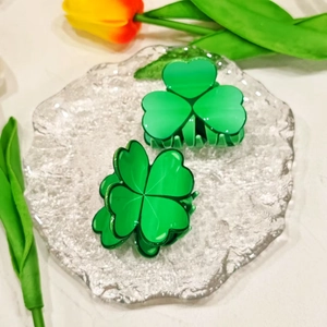 Green acrylic four-leaf clover hair claws on a glass plate with a tulip decorative element