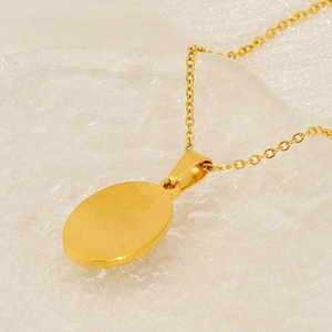 Close-up of gold-plated oval pendant necklace on a decorative textured glass tray