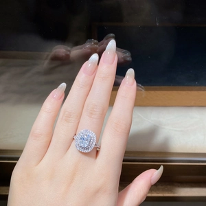 Detail of 4-carat cushion-cut moissanite ring on finger with halo diamond setting