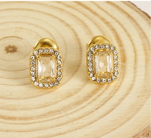 Macro detail of gold double-layer stud earrings with rectangular zircon on wood