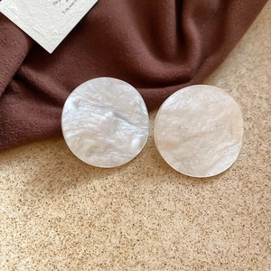 Macro detail of round white acrylic earrings with marble texture on dark fabric