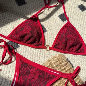 Detail of red floral lace bikini with gold ring hardware on a textured backdrop