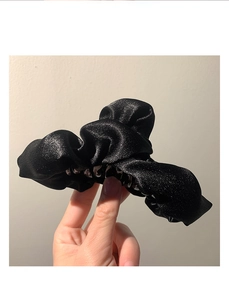 Dettaglio molletta per capelli in raso nero con texture plissettata e punti luce