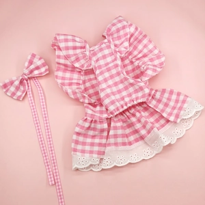 Detail of pink plaid pet dress with lace trim and matching bow headwear on pink background