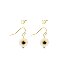 Detail of gold ear jewelry set featuring white round pendants with central black dots