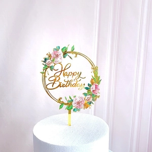 Detail of a floral acrylic cake topper with gold Happy Birthday text and pink flowers
