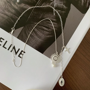 Detail of silver layered necklace with sun flower pendant and white pearl on magazine