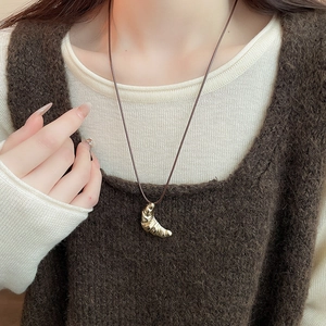 Close-up of golden croissant pendant with leather cord on a white knit sweater
