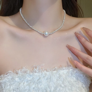 Detail shot of a silver textured necklace featuring a single white pearl on a collarbone