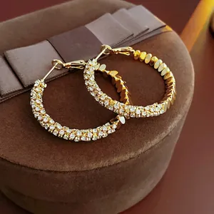 Macro view of gold-tone geometric hoop earrings with multi-row pavé set white crystals