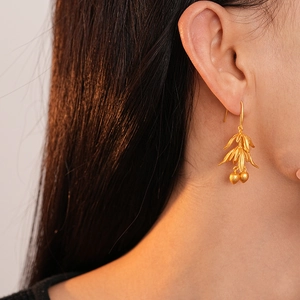 Close-up of matte gold flower leaf earrings with bead charms on a female model