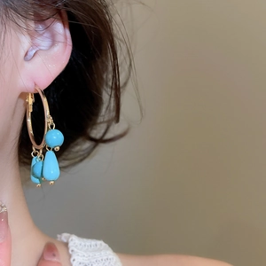 Detailed close-up of golden hoop earrings with turquoise stone tassels in boho style
