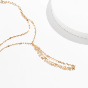 Detail of multi-layered gold body chain with metal bars and elegant tassel on white stand