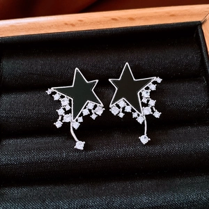 Detail of star-shaped earrings with black enamel inlay and dangling zircon tassels