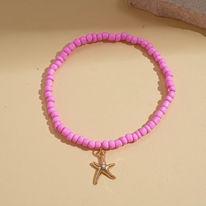 Detailed close-up of pink beaded bracelet with a gold starfish pendant on beach stone background