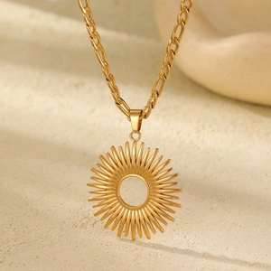 Close-up of gold hollow sunburst pendant on Figaro chain over beige stone background