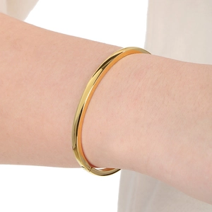 Minimalist 18k gold-plated stainless steel bangle worn on a model's wrist against fabric
