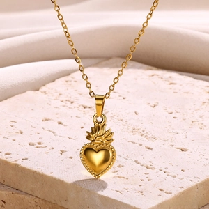 Macro shot of 18k gold heart pendant with crown detail on a textured stone surface