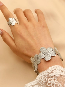 Detailed close-up of a silver flower-shaped bracelet and ring set on a model's hand