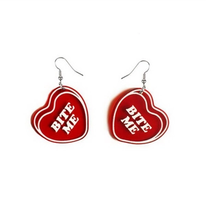 Detail of red heart-shaped acrylic earrings featuring white BITE ME text and silver hooks