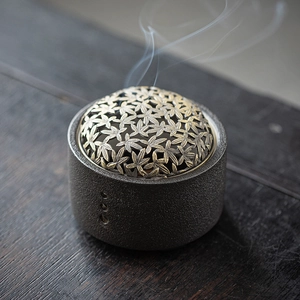 Ceramic incense burner with hollow maple leaf metal lid on dark wooden surface