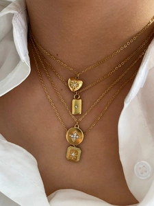 Close-up of layered gold necklaces with heart, star, and geometric pendants on a white shirt