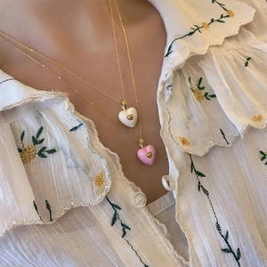 Close-up of layered heart pendant necklace with pink and white enamel on a model