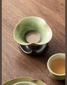Detailed view of kiln-fired ceramic tea strainer with green glaze on a black ceramic base